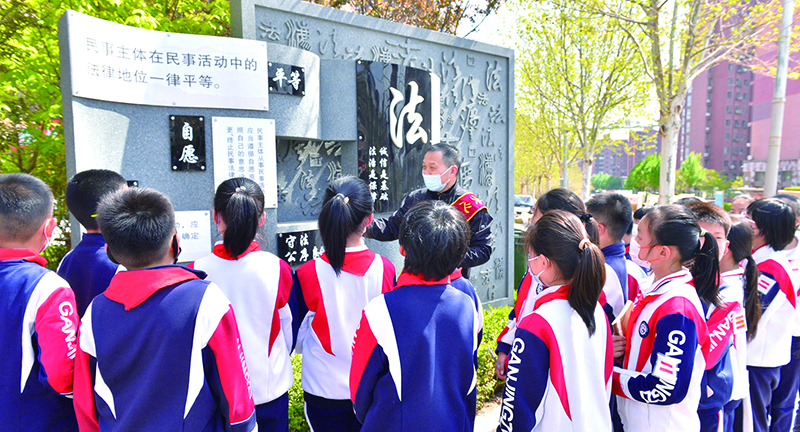 頭題圖，普法志愿者在憲法墻前給學生們普及法律知識。